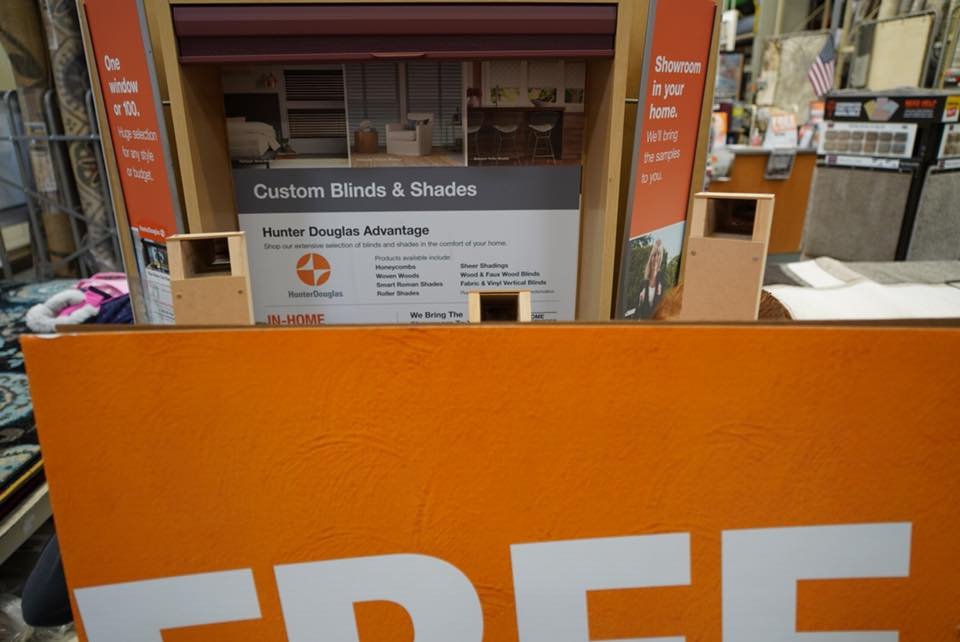 A close-up view of a Home Depot retail display for custom blinds and shades, featuring an orange promotional sign.
