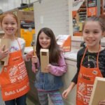 La Push Three children wearing orange aprons holding wooden boards at Home Depot. Another child wearing an apron is shown smiling with a close-up of the apron's 20th anniversary design.