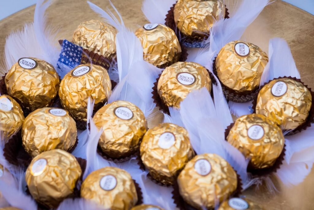 A basket of golden Ferrero Rocher candies nestled in white feathers and blue ribbon.