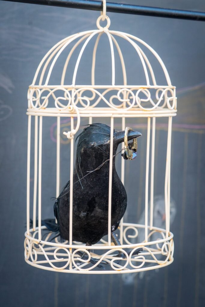A decorative black wire birdcage housing a blackbird sculpture with metallic embellishments.