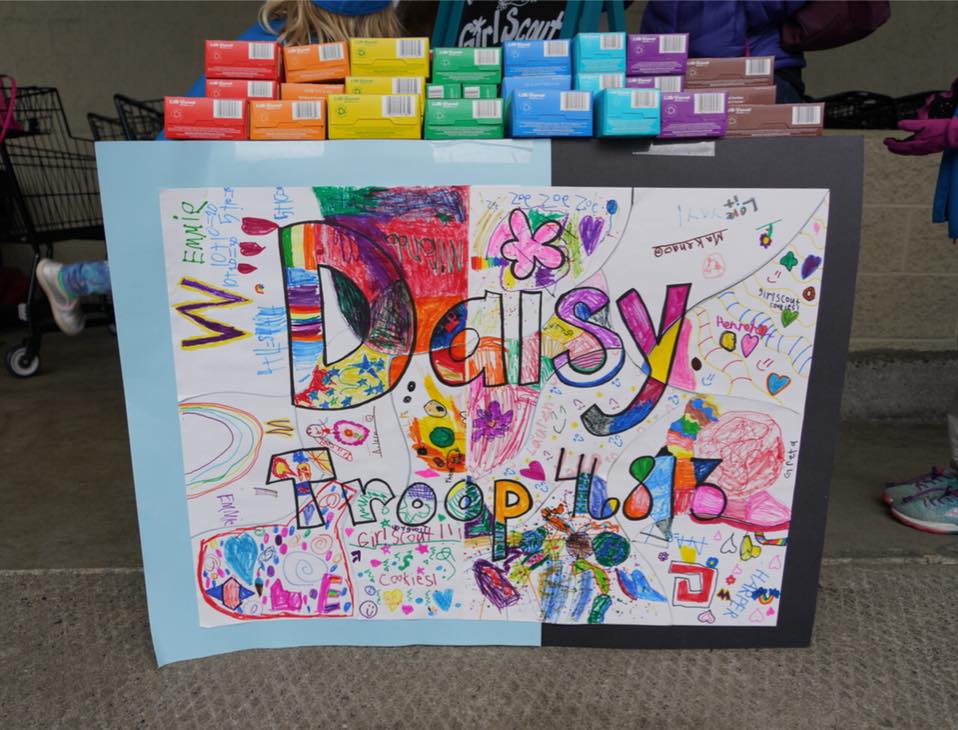 A vibrant child-drawn artwork with the text 'Daisy' is displayed in front of stacks of colorful candy bars.