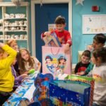 Children gather around a table in a classroom setting, excitedly opening colorful gift bags with Disney characters.