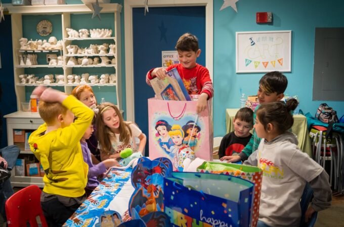 Children gather around a table in a classroom setting, excitedly opening colorful gift bags with Disney characters.