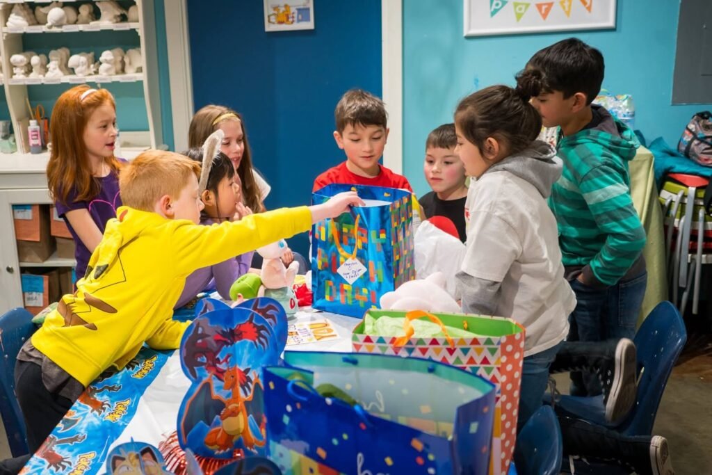 A group of children gather around a table under blue walls to open Christmas presents.