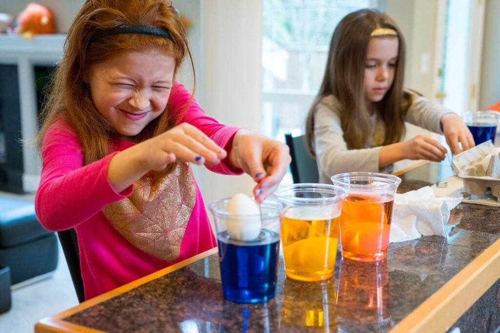 Two children performing a floating egg experiment with colorful water at a kitchen counter. One child looks delighted while observing the results.