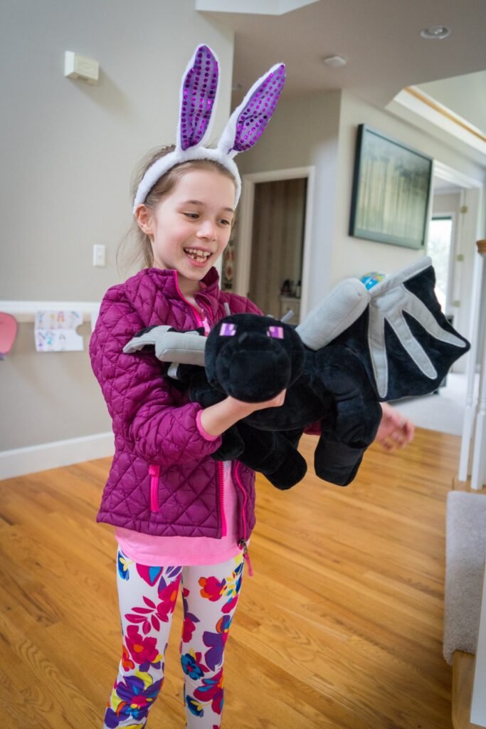 A child wearing purple bunny ears holds a stuffed toy in a home hallway.