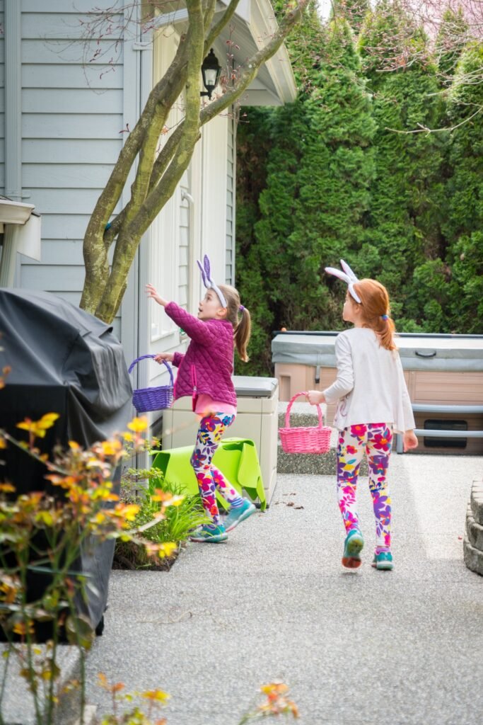 Children in bunny ears hunt for eggs outdoors on a sunny day.