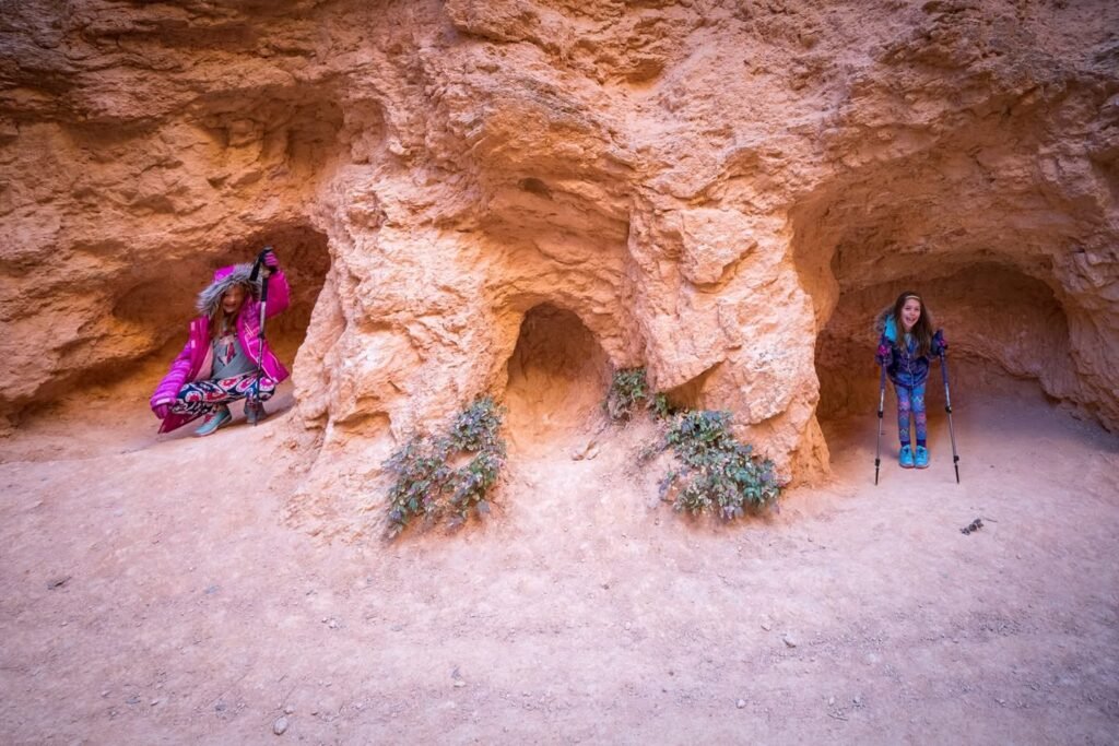 Two people exploring a red sandstone cavern with small desert shrubs.