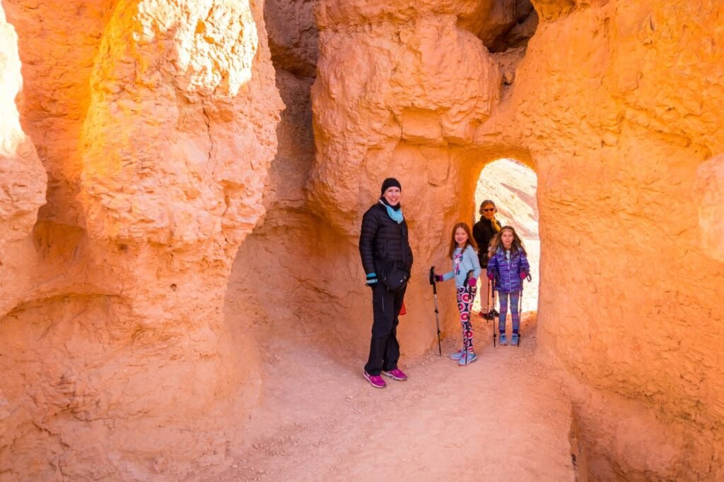 Trekkers standing in a narrow red rock slot canyon with smooth, swirling orange walls.