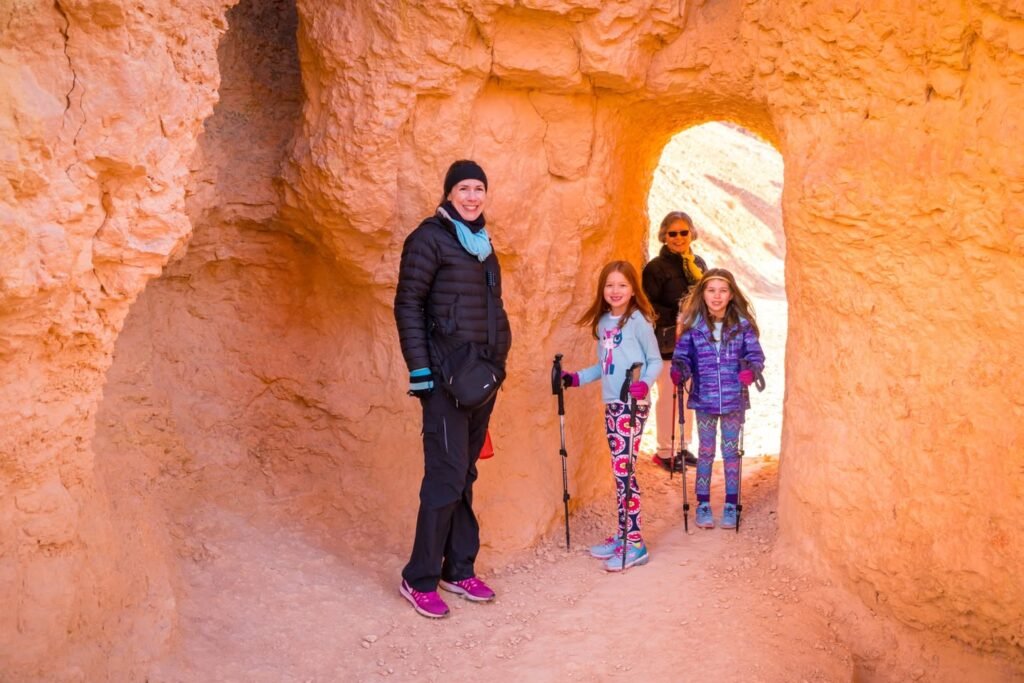 A group of people stands inside a narrow, orange-hued slot canyon. The smooth sandstone walls create a warm and inviting atmosphere.