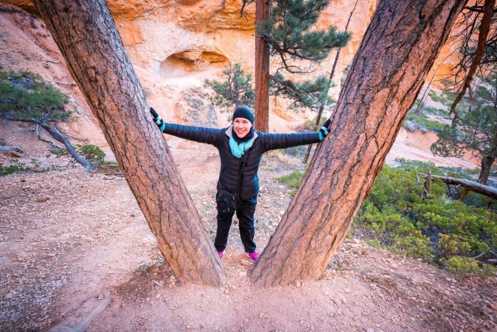 A person standing between two leaning trees with arms spread wide in a rocky natural landscape.
