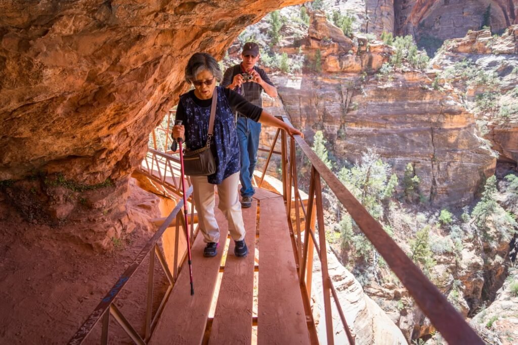 Two hikers walk on a metal walkway beneath the red rock formations of Sedona's Vortex Canyon.