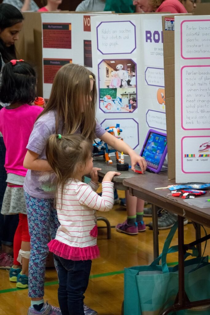 Children interacting with a science fair display board featuring a tablet and written information.