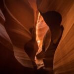 Sunlight illuminates the smooth, curving walls of a narrow desert slot canyon. The warm hues highlight the natural erosion patterns of the sandstone.