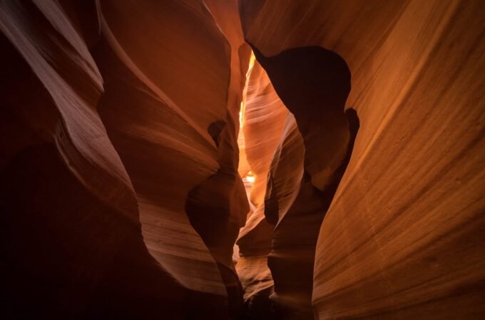 Sunlight illuminates the smooth, curving walls of a narrow desert slot canyon. The warm hues highlight the natural erosion patterns of the sandstone.