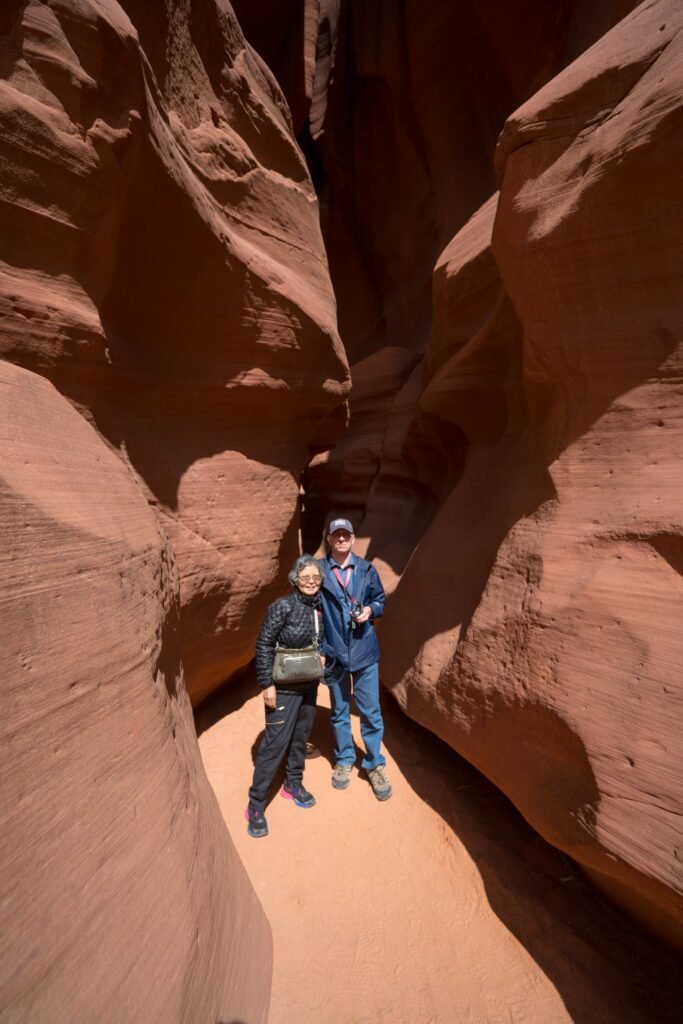 Travelers exploring a narrow, red sandstone slot canyon in the American Southwest.