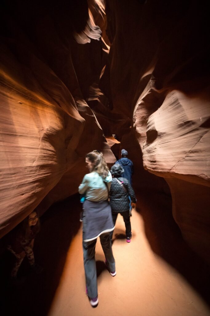 Two hikers exploring the sandstone walls and smooth passages of a narrow slot canyon.