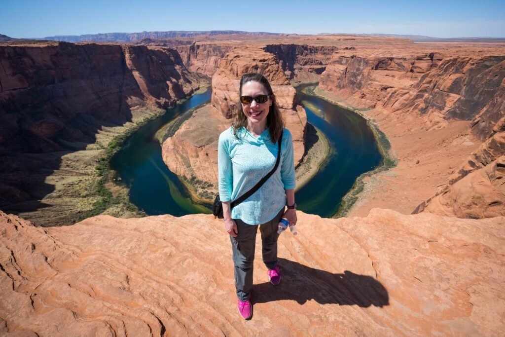 A person stands at the edge of the iconic Horseshoe Bend in the Grand Canyon. Turquoise water winds through rugged red rock formations.