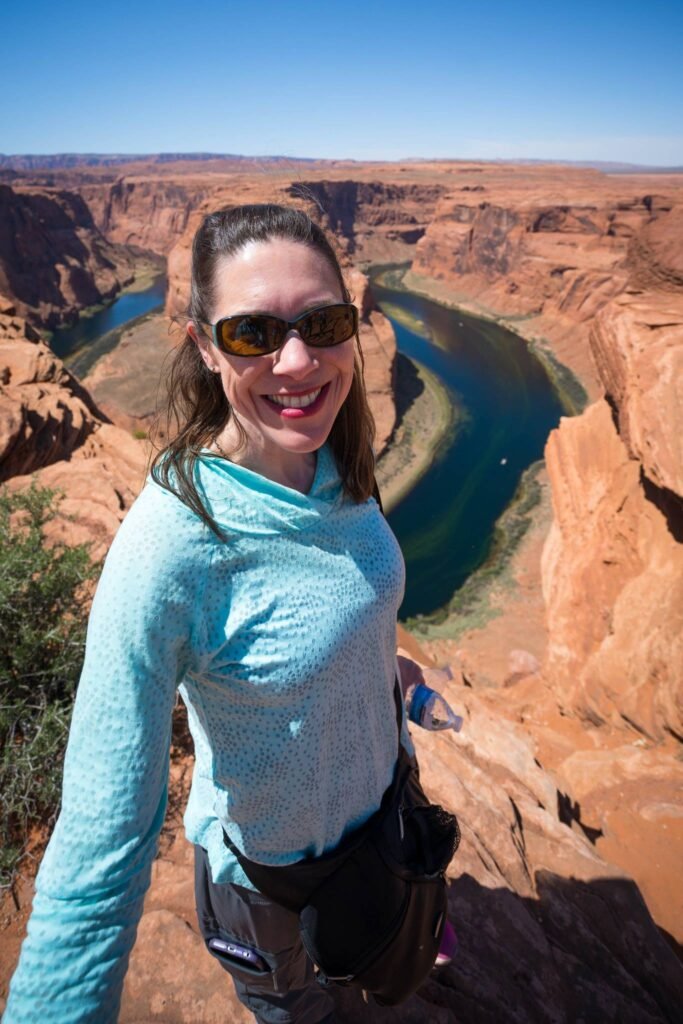 A traveler takes a selfie from the edge of Horseshoe Bend with sweeping canyon views and a winding river below.