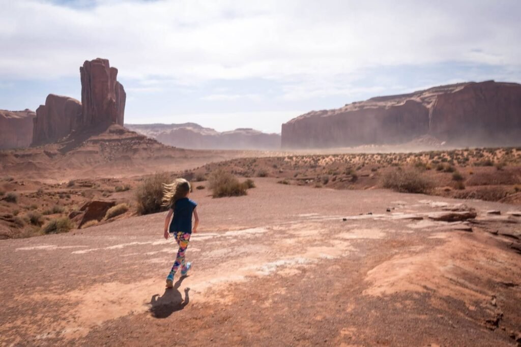 A traveler walks along a dusty desert path towards towering red rock formations at Monument Valley.