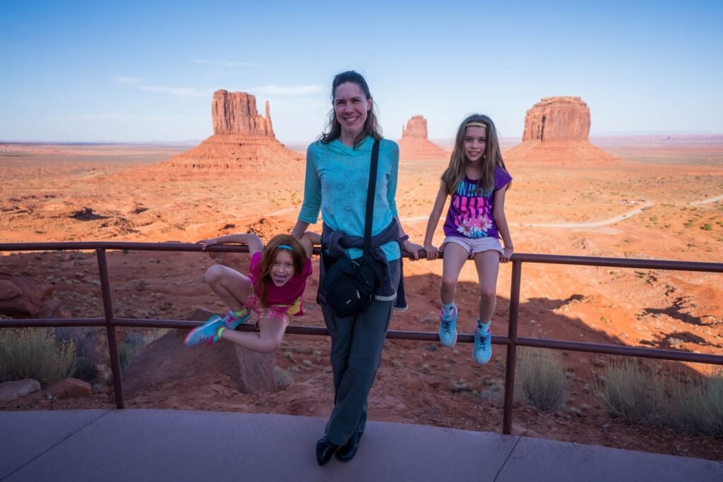A family plays with the iconic sandstone buttes of Monument Basin in Monument Valley as the backdrop at sunset.