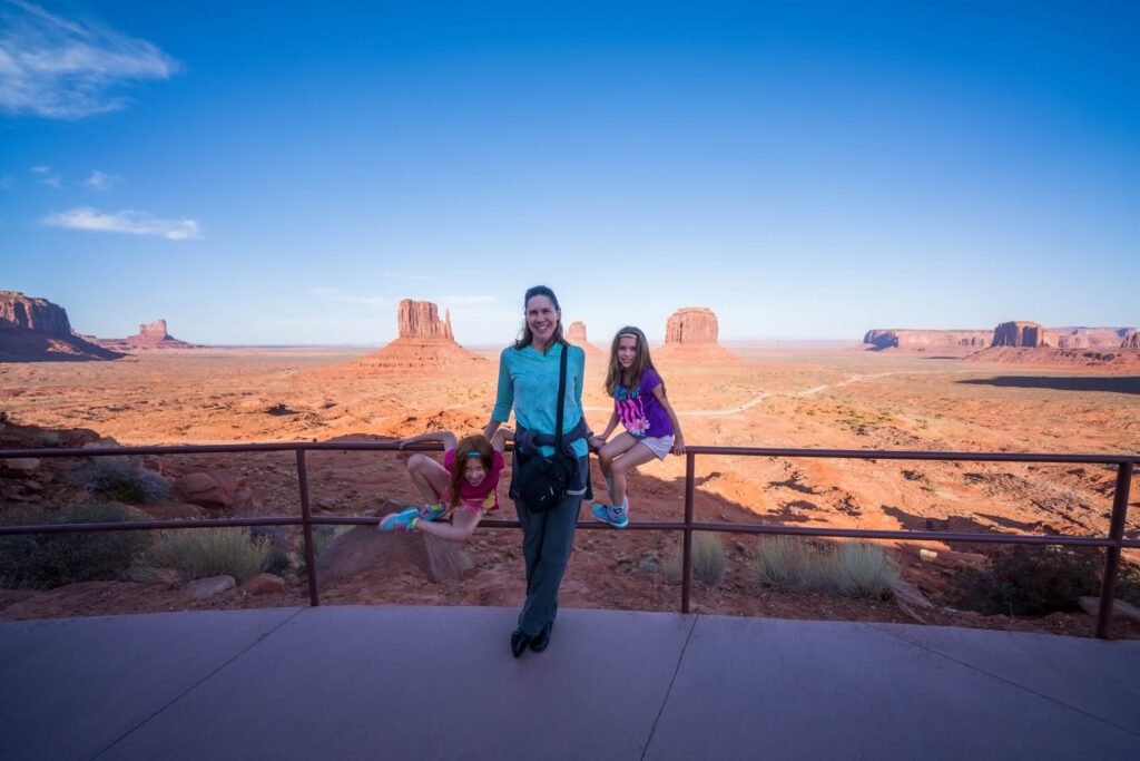 A family poses for a photo against the red rock formations of Canyonlands National Park. Clear blue skies overlook the vast desert landscape and iconic mesas.