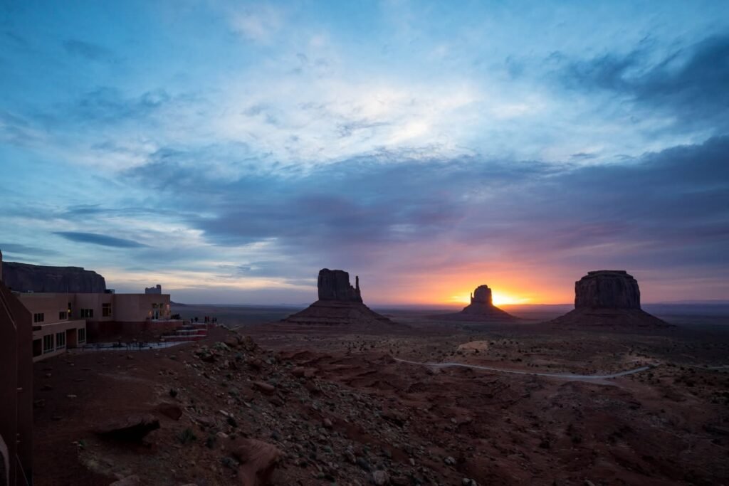 Sunset over Monument Valley's iconic rock formations, viewed from a nearby hotel with warm orange skies.