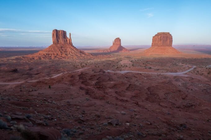A wide-angle view of desert mesas and buttes at twilight, facing a distant plateau.