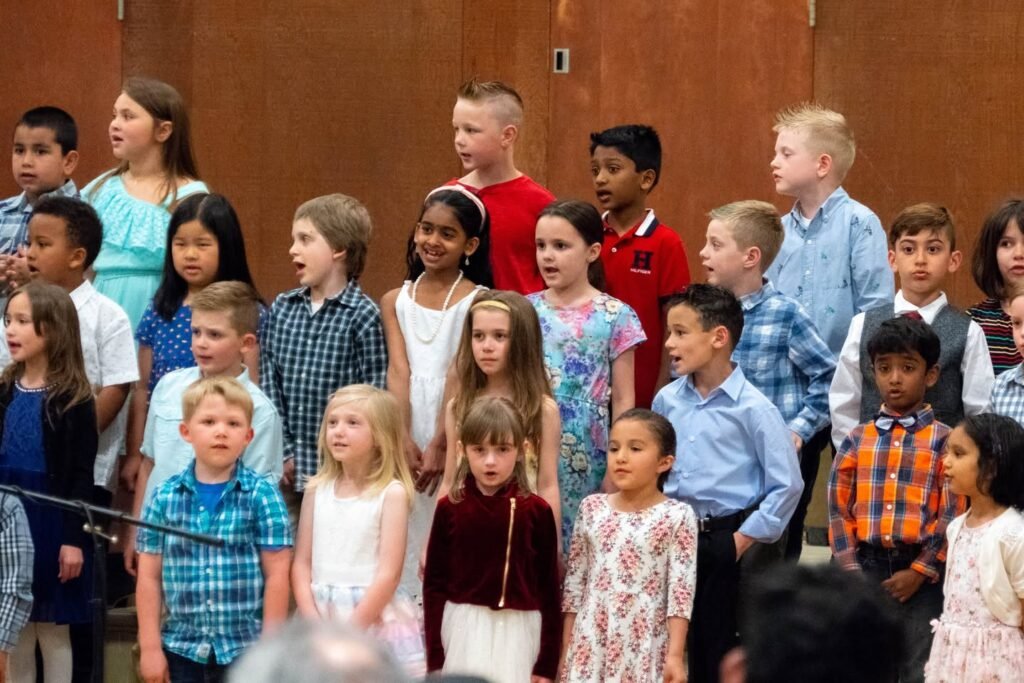 A diverse group of children singing together as a choir against a wooden backdrop.