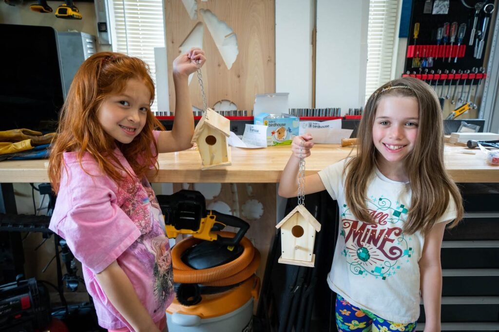 Two people proudly showing handmade wooden birdhouses with a workbench and tools in the background.