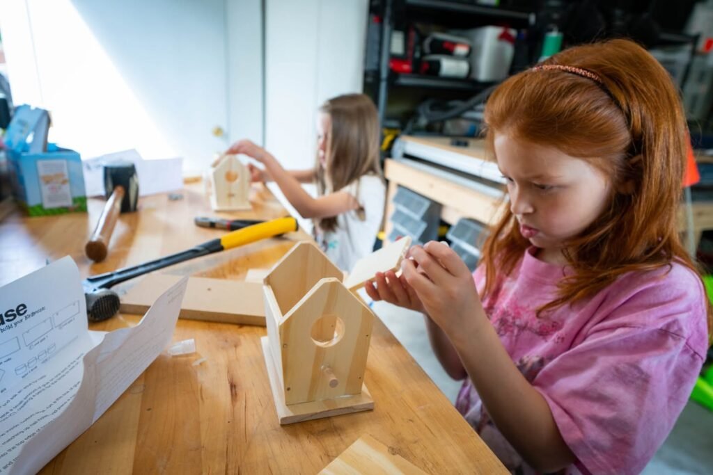 Kids assembling wooden birdhouses at a table with instructions and tools nearby