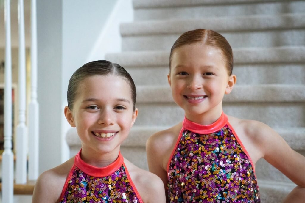 Two smiling sisters wear matching sequined leotards on the stairs.