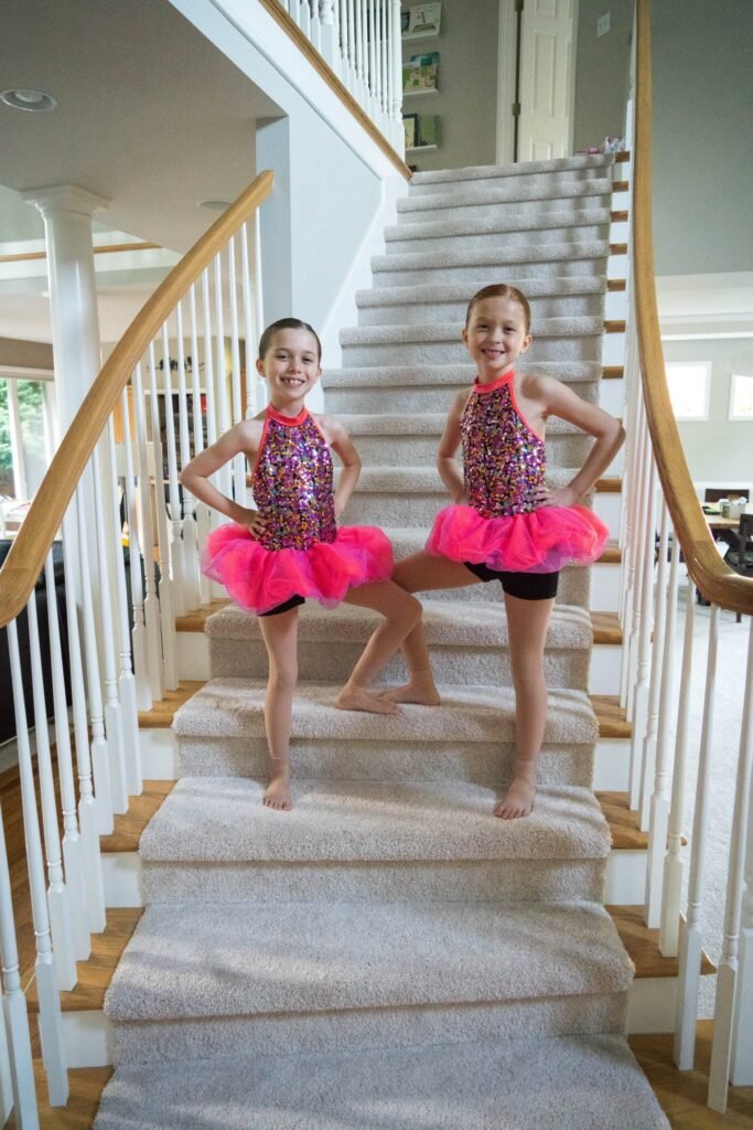 Children in pink ballet tutus standing on a carpeted staircase.