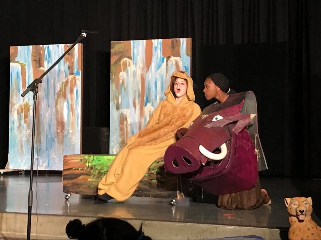A young performer in a yellow robe next to a person in a pig costume on a stage.