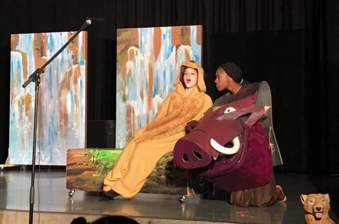 A young performer in a yellow robe next to a person in a pig costume on a stage.