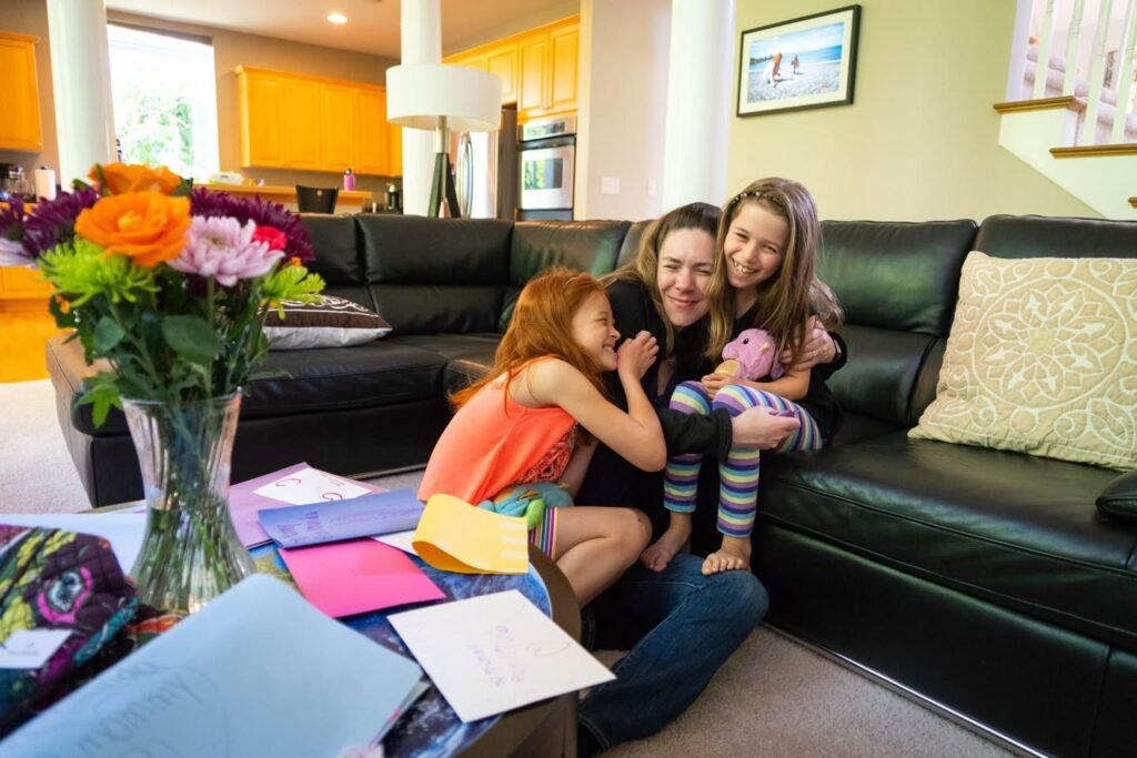 A woman and two children share a moment on a black leather sofa in a modern home living room.