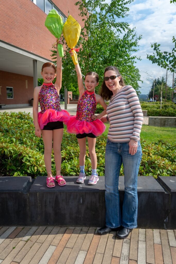 A family enjoys a sunny day outdoors while kids in dance costumes hold balloons after a performance.