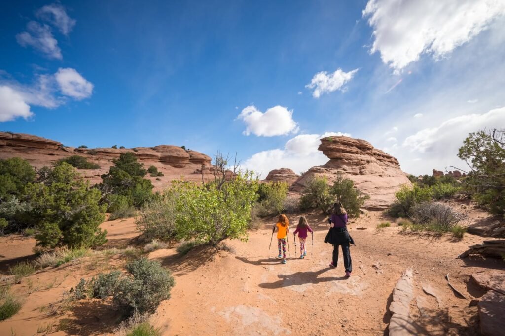 A group walking along a sandy path through red rock formations under a beautiful blue sky.