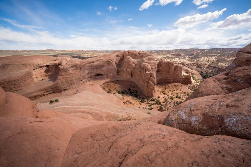 A panoramic view of rugged desert rock formations under a clear blue sky with scattered clouds.