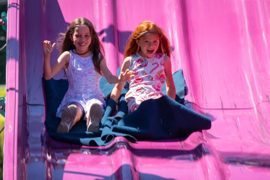 Two kids enjoy sliding down a bright pink inflatable slide.