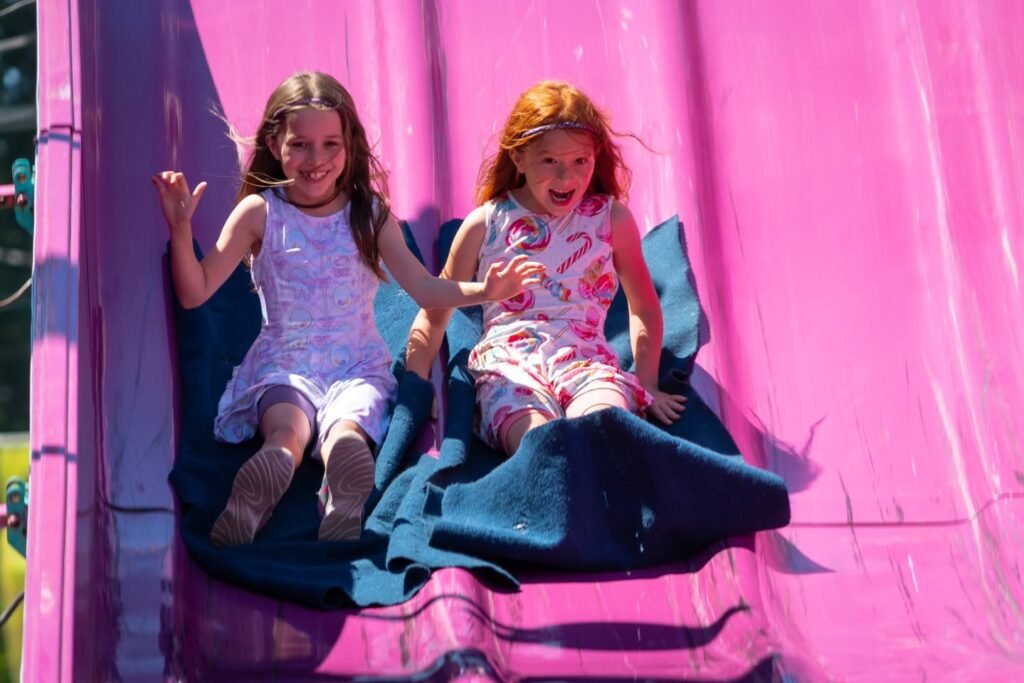 Two kids sliding down a light pink playground slide