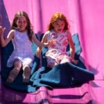 New Bikes Two kids sliding down a light pink playground slide