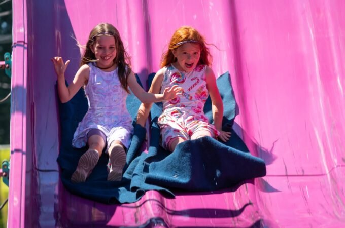 Two kids sliding down a light pink playground slide
