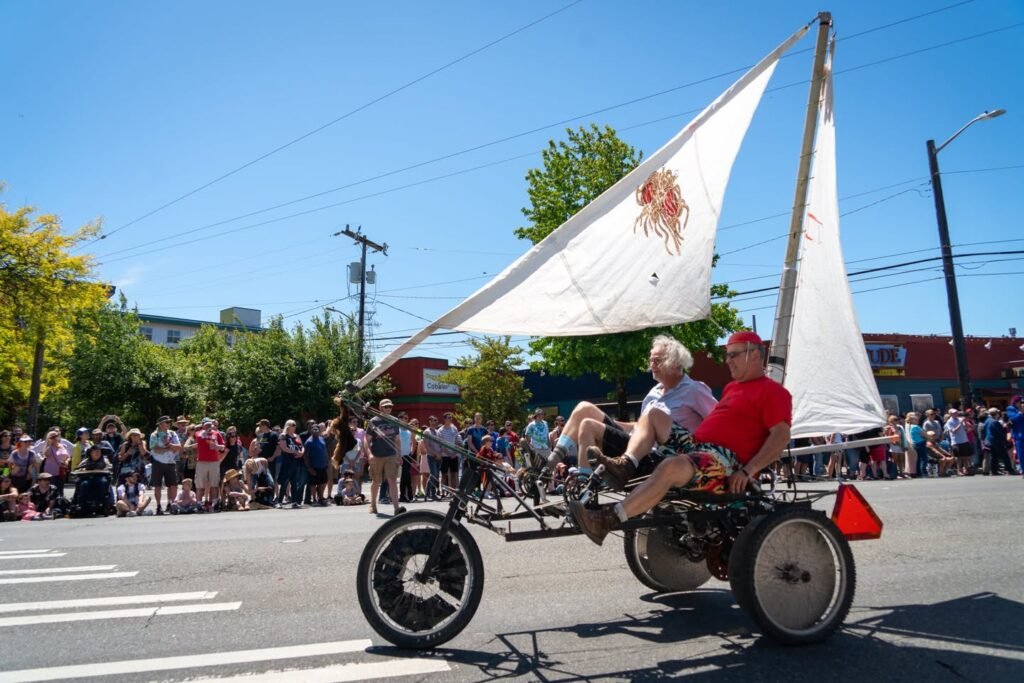 A wind-powered vehicle with sails in a street parade, with a crowd watching.