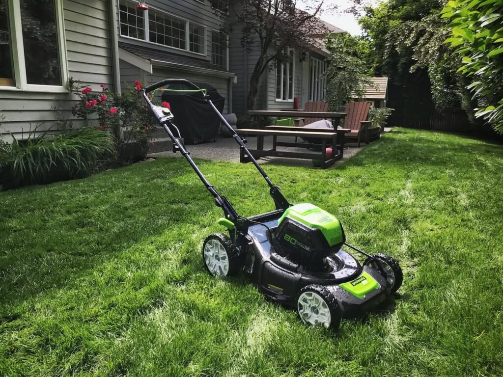 A green push mower rests on a well-manicured lawn in front of a house. Compact and ready for yard work.