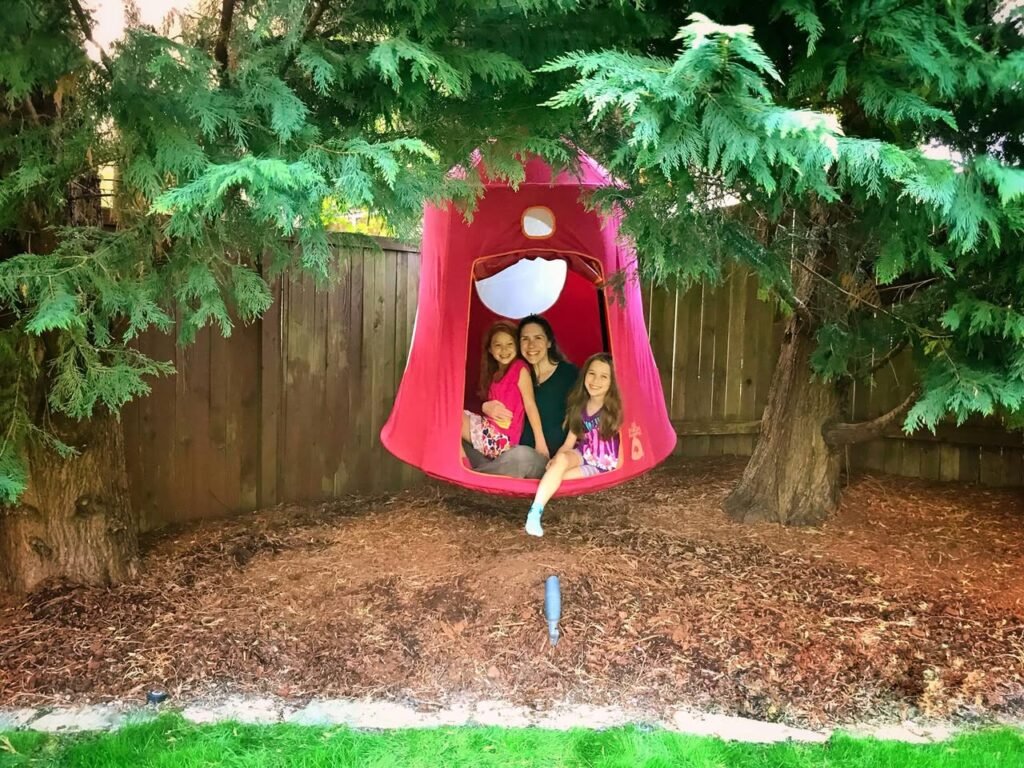 Family enjoying time together in a red garden swing surrounded by greenery and a wooden fence.