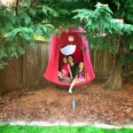 Bakersfield Family enjoying time together in a red garden swing surrounded by greenery and a wooden fence.