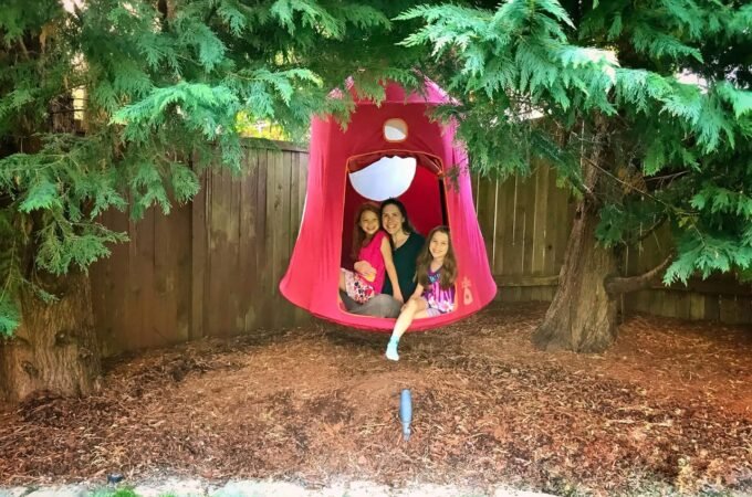 Family enjoying time together in a red garden swing surrounded by greenery and a wooden fence.