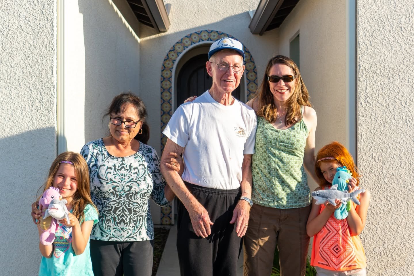 Bakersfield A family of five posing for a photo in front of an adorable building. The two young girls are each holding a stuffed animal.