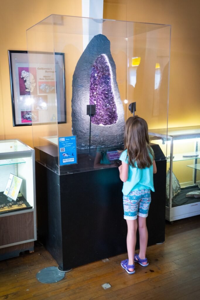 A young visitor inspects a large purple geode display in a museum setting, captured in a portrait photo.
